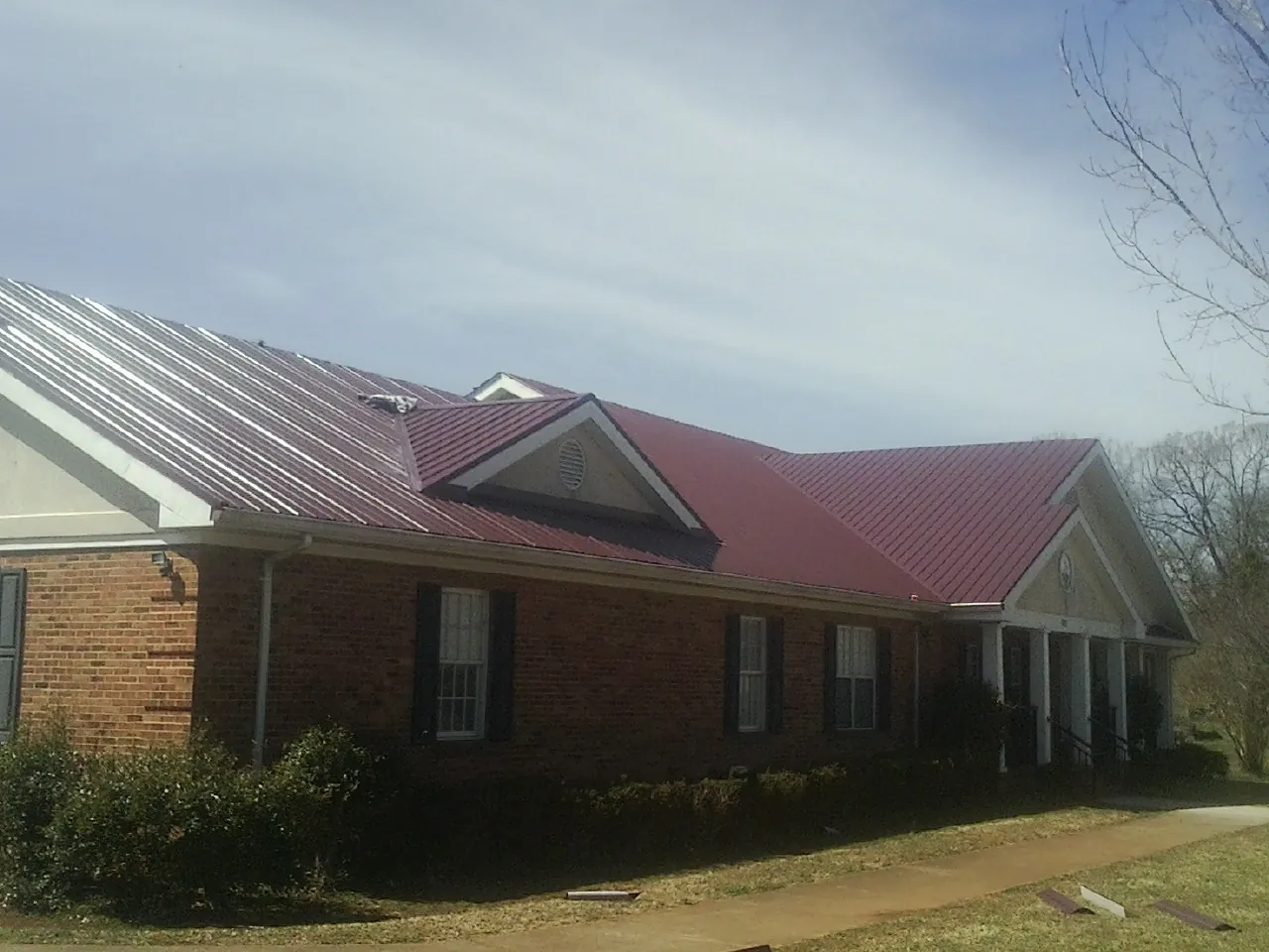 Red metal roof with gabled entries on a long brick building, from a Hail Damage Roof Repair job in Rockville