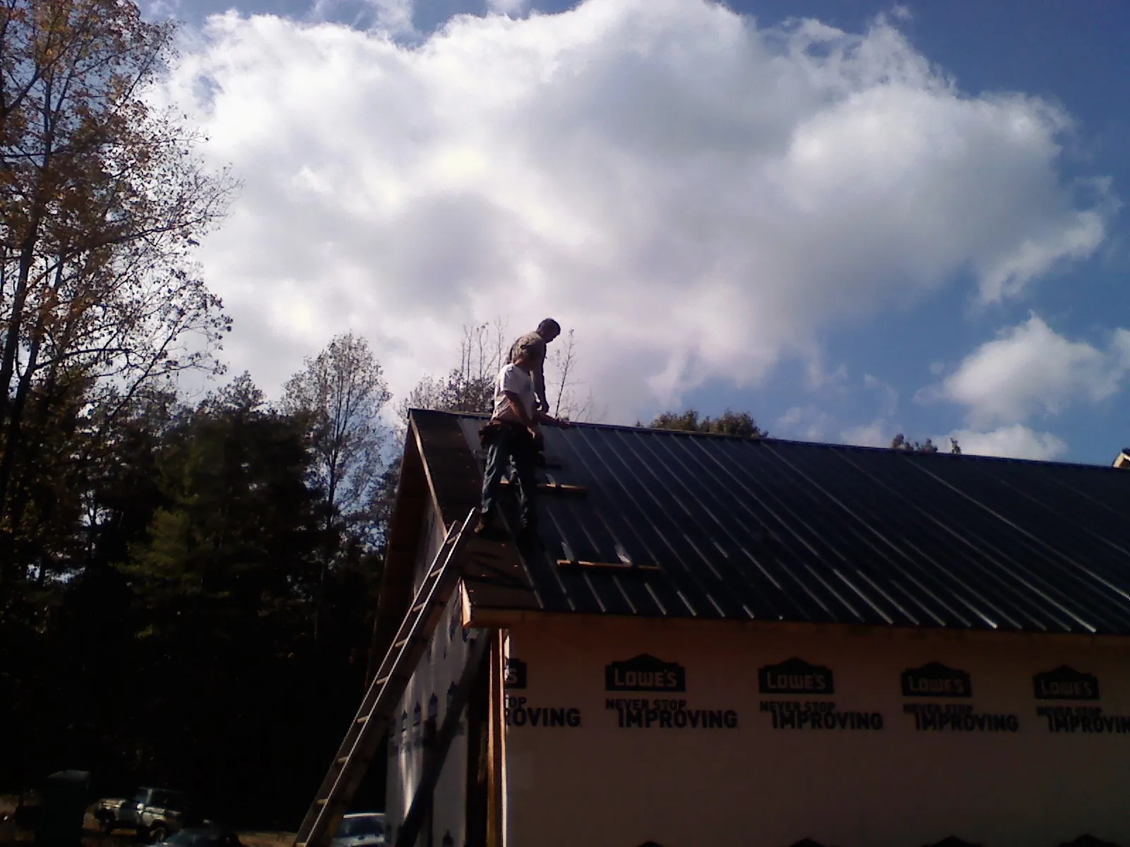 Roofer fastening dark metal panels high against a cloudy sky, from a Roof Inspection job in Rockville